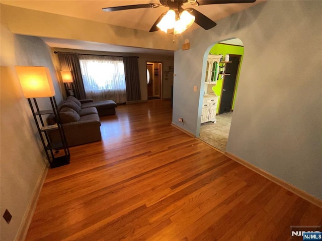 unfurnished living room featuring arched walkways, ceiling fan, baseboards, and wood finished floors