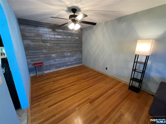 interior space featuring an accent wall, a ceiling fan, wooden walls, wood finished floors, and baseboards