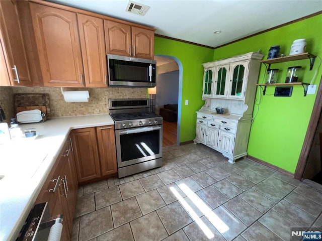 kitchen featuring arched walkways, stainless steel appliances, light countertops, visible vents, and backsplash