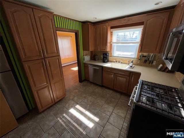 kitchen featuring a baseboard radiator, a sink, light countertops, appliances with stainless steel finishes, and tasteful backsplash