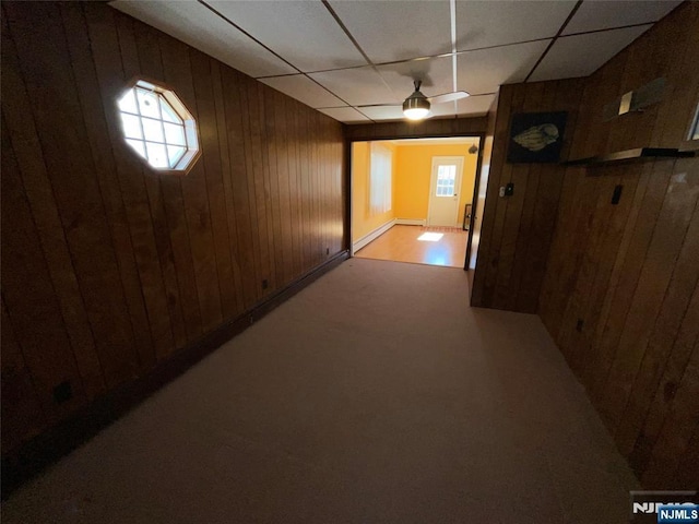 corridor featuring a baseboard heating unit, a drop ceiling, and wood walls