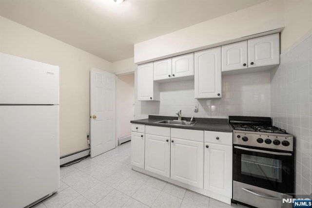 kitchen featuring dark countertops, baseboard heating, freestanding refrigerator, stainless steel range with gas stovetop, and a sink