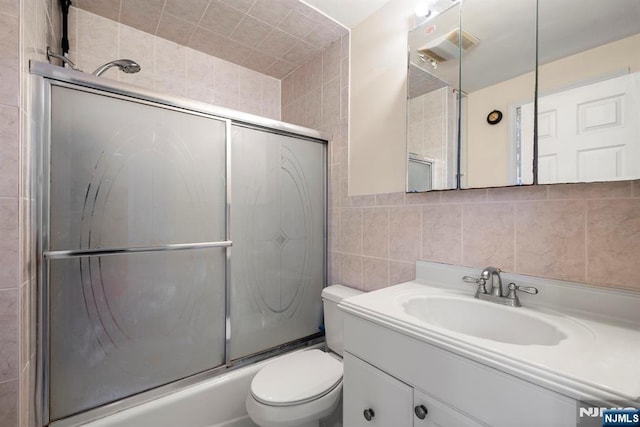 full bathroom featuring enclosed tub / shower combo, toilet, tile walls, and vanity