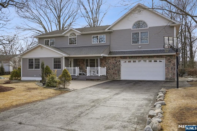 traditional-style house with covered porch, stone siding, aphalt driveway, and an attached garage