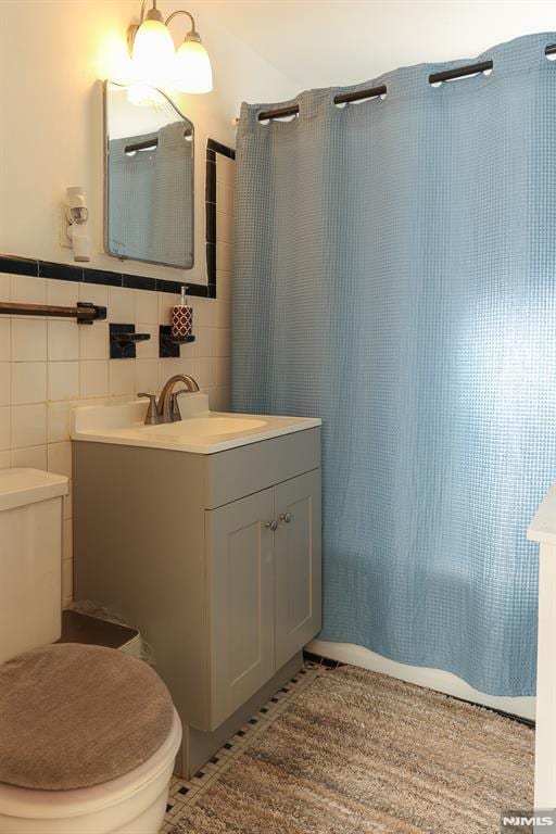 bathroom with toilet, curtained shower, tile patterned flooring, vanity, and tile walls