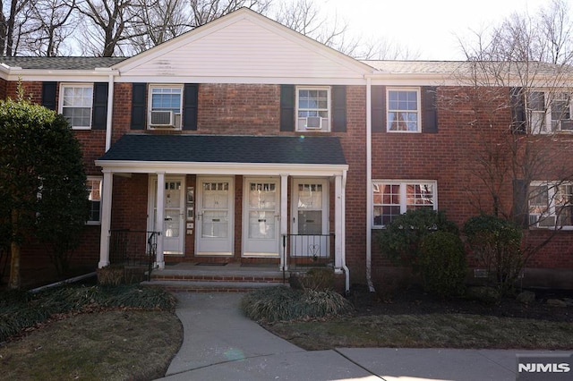 townhome / multi-family property with a porch, cooling unit, and brick siding