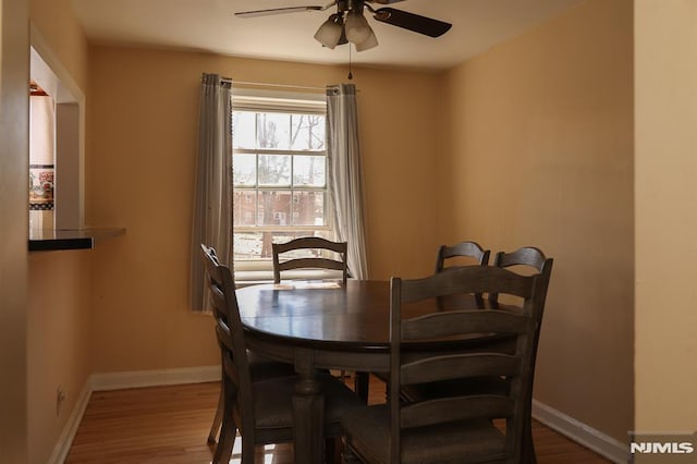 dining area with wood finished floors, a ceiling fan, and baseboards