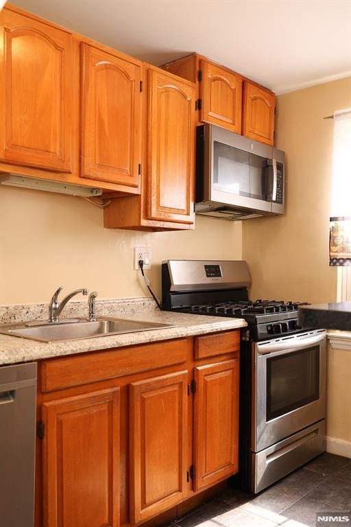 kitchen featuring appliances with stainless steel finishes, a sink, and brown cabinets