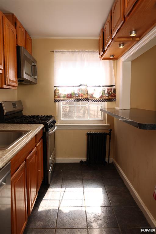 kitchen with stainless steel appliances, radiator heating unit, brown cabinetry, and baseboards