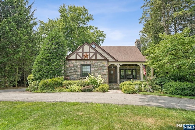 tudor house featuring stone siding, roof with shingles, and a chimney