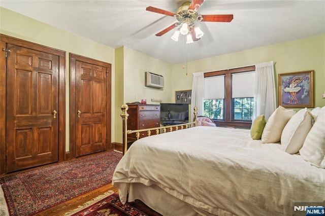 bedroom featuring a wall unit AC, ceiling fan, multiple closets, and wood finished floors