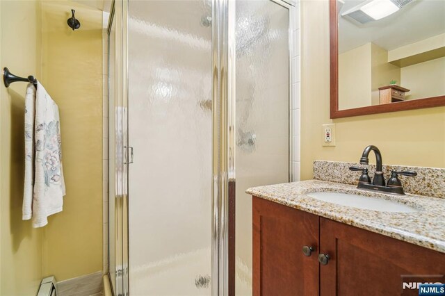 bathroom featuring a baseboard radiator, vanity, and a shower stall