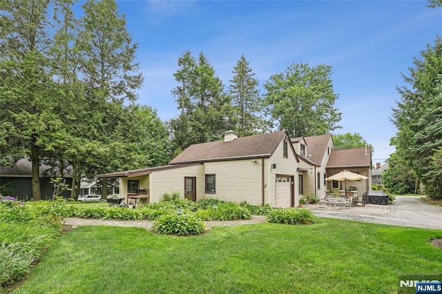 view of front facade featuring a patio, a front yard, driveway, and a garage