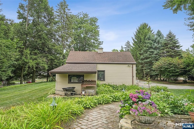 view of home's exterior with a chimney, a yard, and a shingled roof