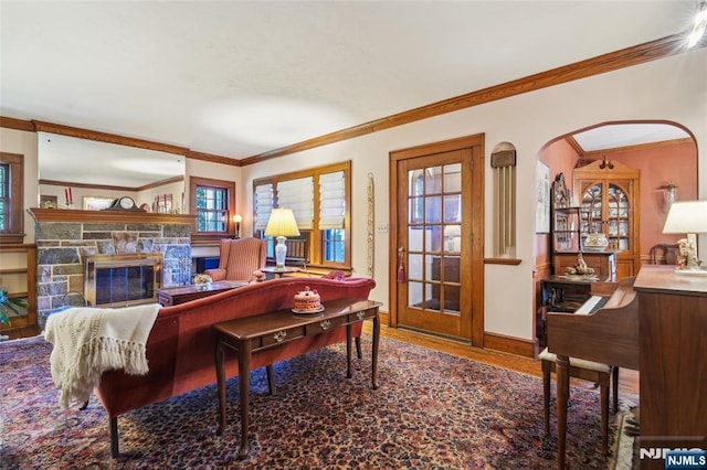 living room featuring a stone fireplace, crown molding, wood finished floors, and baseboards