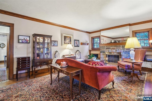 living area with a stone fireplace, wood finished floors, baseboards, and ornamental molding