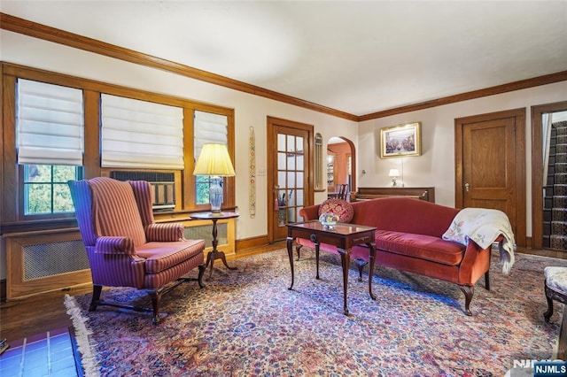 living area featuring wood finished floors, baseboards, arched walkways, and ornamental molding