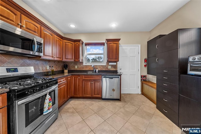 kitchen with brown cabinets, stainless steel appliances, decorative backsplash, light tile patterned flooring, and a sink