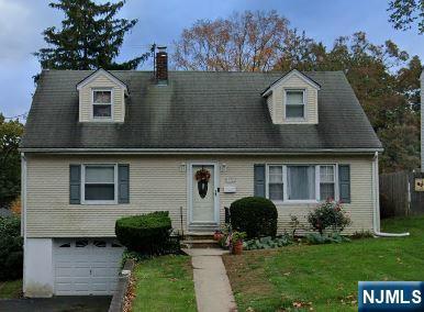 cape cod home with aphalt driveway, entry steps, a front yard, a chimney, and a garage