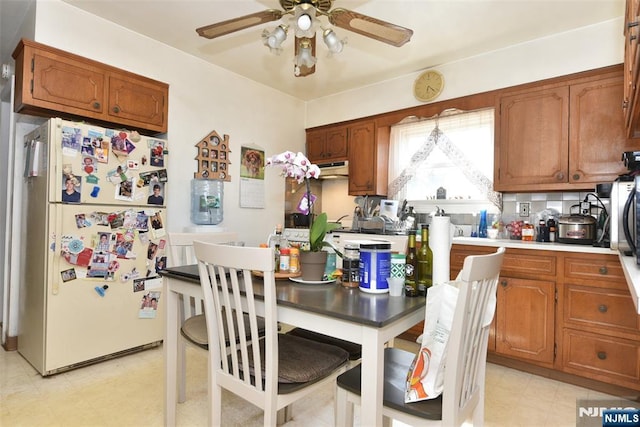 kitchen with brown cabinetry, a ceiling fan, light floors, freestanding refrigerator, and light countertops