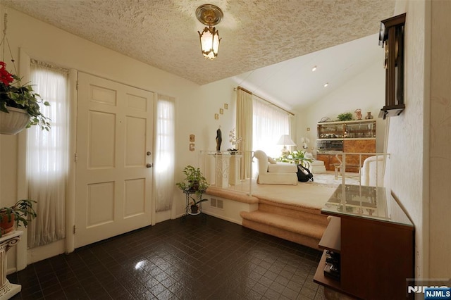 foyer entrance featuring lofted ceiling, visible vents, and a textured ceiling