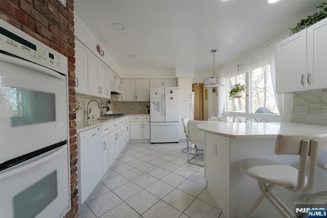 kitchen featuring white appliances, decorative backsplash, a breakfast bar, a peninsula, and light countertops