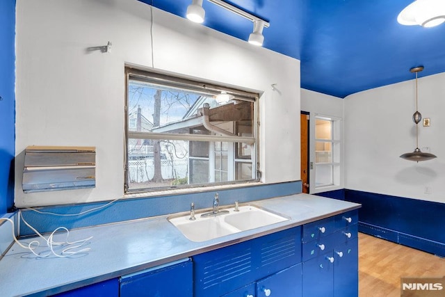 kitchen with a sink, light countertops, blue cabinetry, light wood finished floors, and rail lighting