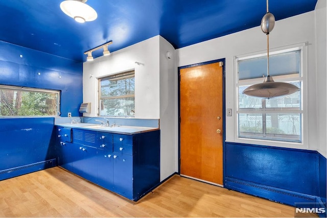 kitchen with blue cabinetry, light countertops, light wood-style flooring, a baseboard heating unit, and a sink