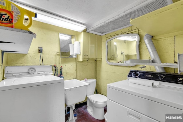 washroom featuring concrete block wall, laundry area, washing machine and dryer, and a sink