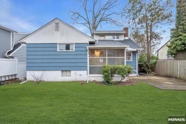 rear view of property featuring a yard, a chimney, and fence