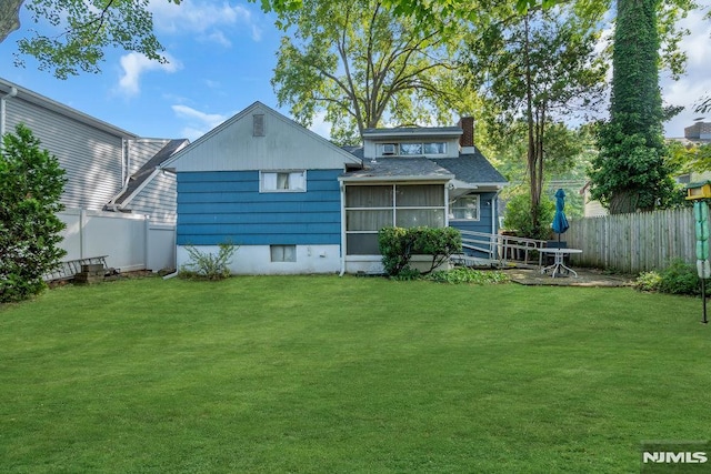 back of property featuring a sunroom, a lawn, a chimney, and fence