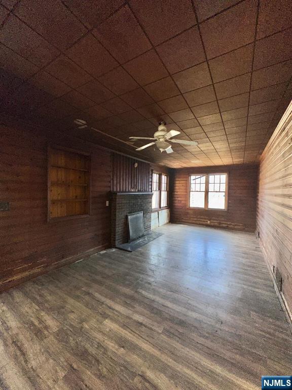 unfurnished living room featuring wood walls, a fireplace, wood finished floors, and a ceiling fan