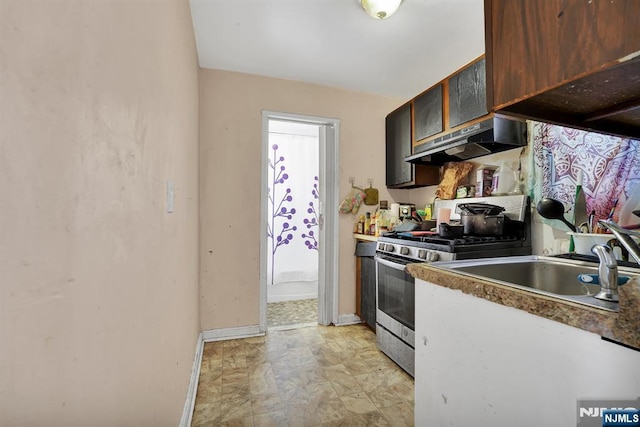 kitchen with baseboards, a sink, under cabinet range hood, and stainless steel gas range oven