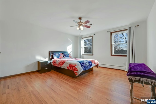 bedroom with a baseboard radiator, multiple windows, baseboards, and light wood-style flooring