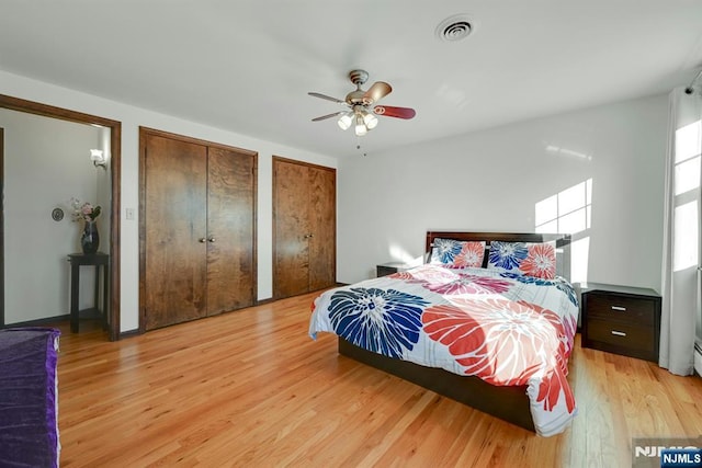 bedroom with visible vents, ceiling fan, light wood-style floors, and multiple closets