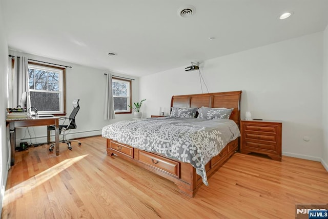 bedroom with light wood-style floors, visible vents, baseboard heating, and baseboards