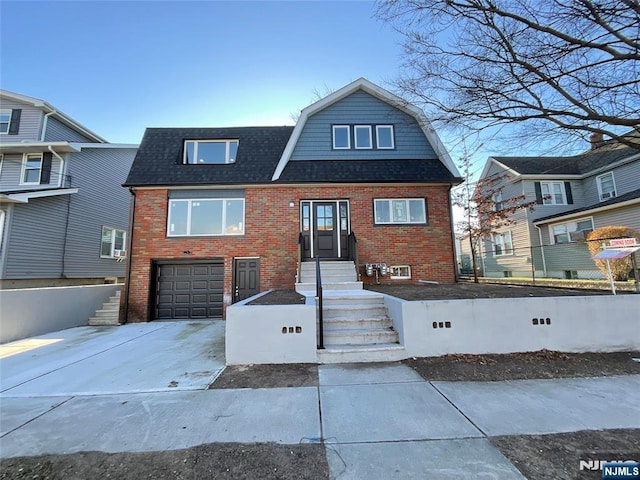 view of front of property with brick siding, roof with shingles, concrete driveway, an attached garage, and a gambrel roof