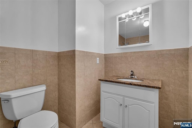 bathroom with a wainscoted wall, tile walls, toilet, and vanity