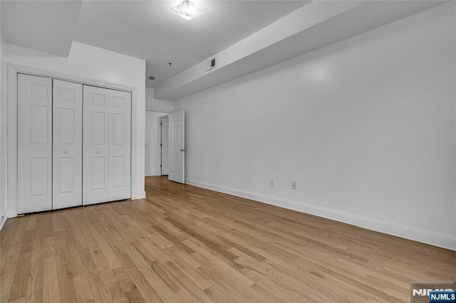 unfurnished bedroom featuring light wood-style floors, baseboards, visible vents, and a closet