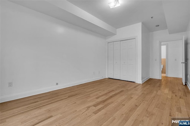 unfurnished bedroom with light wood-type flooring, baseboards, and a closet