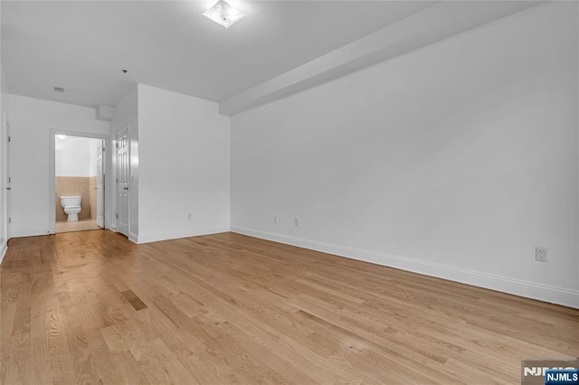 unfurnished bedroom with light wood finished floors, baseboards, and ensuite bathroom