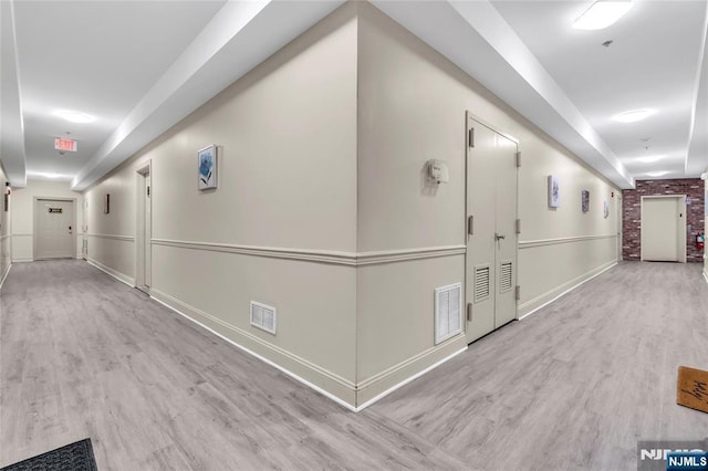 hall with wood finished floors, visible vents, and baseboards