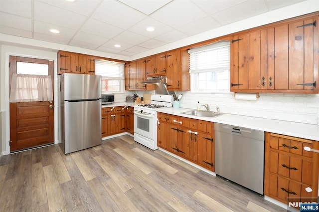 kitchen featuring brown cabinetry, light wood-style flooring, stainless steel appliances, under cabinet range hood, and a sink