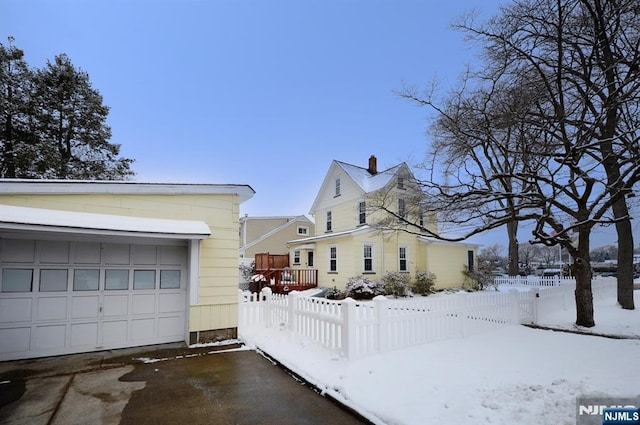 view of snowy exterior featuring a garage, driveway, and fence