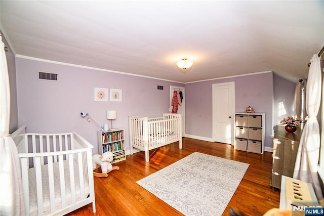 bedroom featuring baseboards, wood finished floors, visible vents, and crown molding