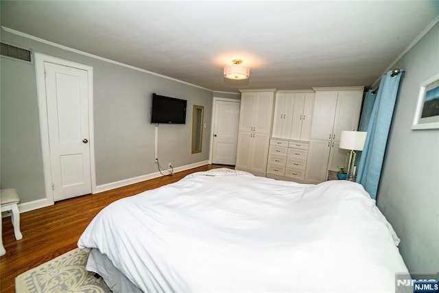 bedroom with wood finished floors, visible vents, multiple closets, baseboards, and crown molding