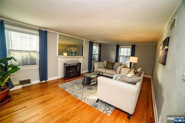 living area with baseboards, visible vents, a fireplace with raised hearth, and wood finished floors