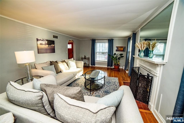 living room with arched walkways, crown molding, a fireplace, visible vents, and wood finished floors