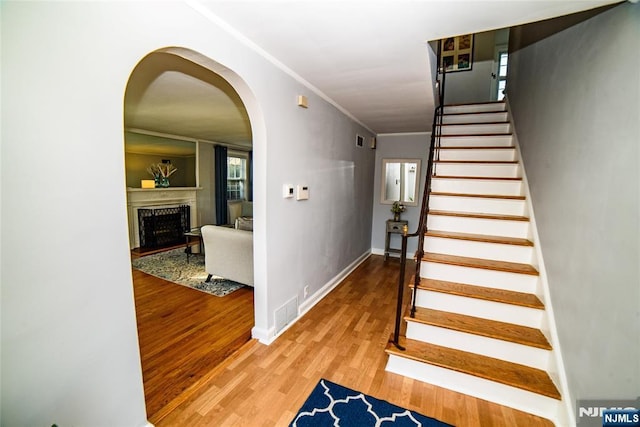 stairway with arched walkways, ornamental molding, a fireplace, and wood finished floors