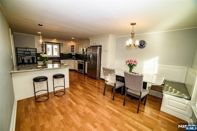 kitchen featuring stainless steel appliances, light wood finished floors, a peninsula, and a kitchen bar